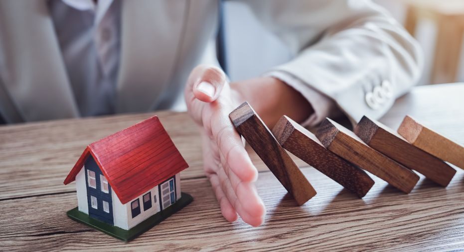 hand prevents a series of blocks from falling on a blue and white house with red roof