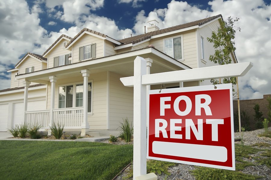 White house on green lawn with red sign stating For Rent